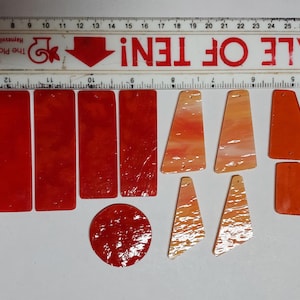 May include: A collection of red and orange acrylic jewelry components arranged next to a ruler. The set includes four rectangular pieces, one circular piece, four trapezoidal pieces, and four smaller trapezoidal pieces, all with small holes.