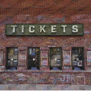 May include: A brick building with a "TICKETS" sign above five ticket windows. The sign has illuminated letters. The brick wall is covered in graffiti. The windows have posters and are framed in dark green.