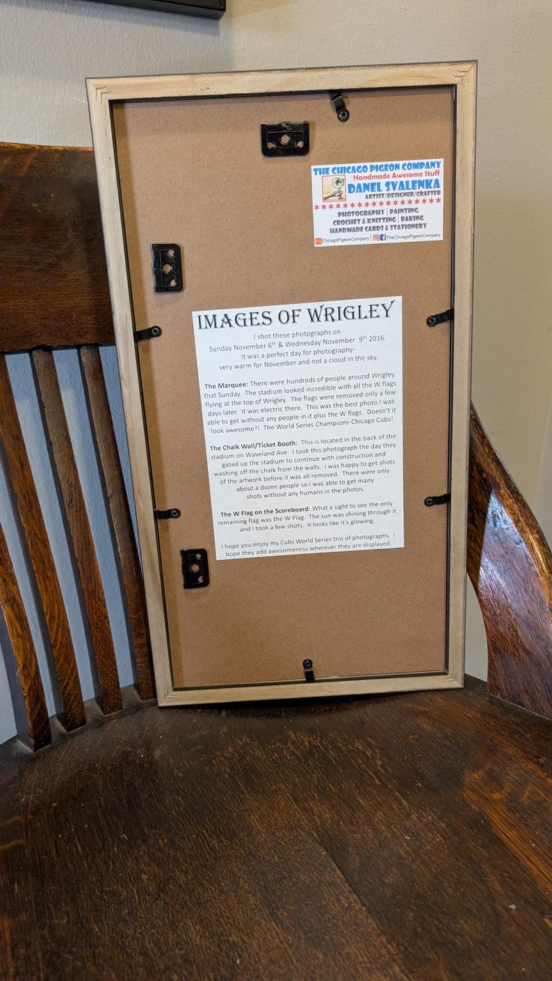 May include: Framed print titled "Images of Wrigley" with text about photographs taken at Wrigley Field. The frame is light brown, and the print includes text and a logo for The Chicago Pigeon Company.
