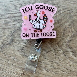 May include: A pink glittery badge reel featuring a cartoon goose dressed as a medical professional with a stethoscope, holding a syringe and a prescription bottle. The text reads ICU GOOSE ON THE LOOSE, surrounded by small colorful flower icons.