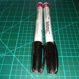 May include: Two black Sharpie permanent markers with white labels. The labels feature the Sharpie brand name and the words "Permanent Marker" printed on them.