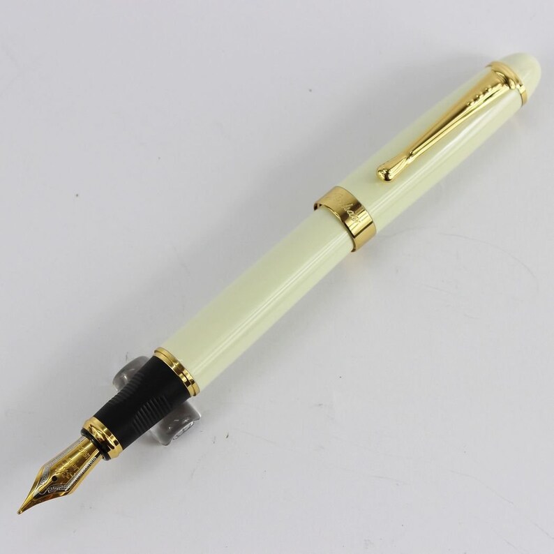 May include: A white fountain pen with gold accents and a black grip. The pen has a classic design and is made of high-quality materials.