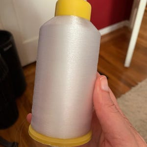 May include: A spool of white thread with a yellow plastic top and bottom. The thread is wound tightly around the spool.