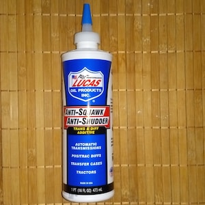 Könnte beinhalten: Eine blaue und weiße Flasche mit Lucas Oil Products Inc. Anti-Squawk Anti-Shudder Getriebe- und Differentialadditiv. Die Flasche ist für den Einsatz in Automatikgetrieben, Posi-Trac-Differentialen, Verteilergetrieben und Traktoren gekennzeichnet. Die Flasche enthält 1 Pint (16 Flüssigunzen) oder 473 ml.