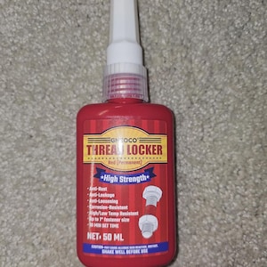 May include: A red bottle of thread locker with a white applicator tip. The label reads "THREAD LOCKER" and lists features like anti-rust and high strength. The bottle contains 50 ml.