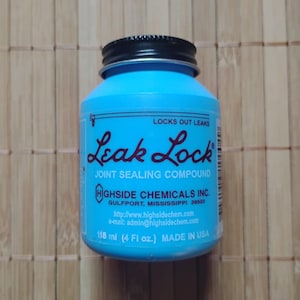 Puede incluir: Una botella cilíndrica azul con una tapa negra etiquetada "Leak Lock Joint Sealing Compound" de Highside Chemicals Inc. La botella contiene 118 ml y está hecha en los Estados Unidos.