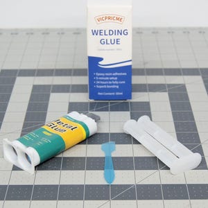 Pode incluir: Um conjunto de cola epóxi de duas partes para metal, com um rótulo azul e amarelo, um aplicador branco, um espalhador de plástico azul e uma caixa de cola para soldar. A caixa é azul e branca e diz "VICPRICME WELDING GLUE".