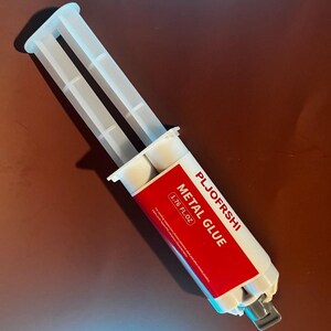 May include: A white plastic tube with a red label that says "PLJOFERSHI METAL GLUE 1.76 FL OZ".