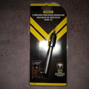 Può includere: Un incisore di precisione senza fili argentato con punta rivestita di diamante. La confezione è nera con strisce gialle e il testo "GENERAL CORDLESS PRECISION ENGRAVER GRAVEUR DE PRÉCISION SANS FIL No. 505" è stampato sul davanti. L'incisore è confezionato con due batterie.