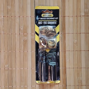 Puede incluir: Un kit de ojales de latón de 1,27 cm con una herramienta de instalación. El paquete es amarillo y negro con el texto "General 1/2" Brass Grommet Kit Rust-Free Guarantee".
