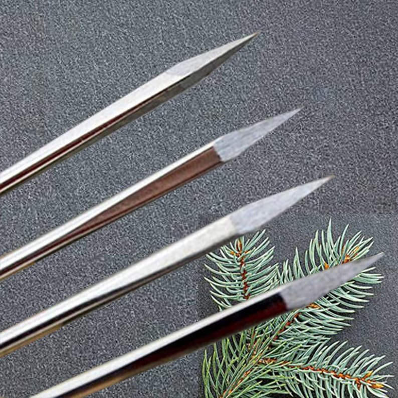May include: Four silver metal knitting needles with pointed tips. The needles are arranged in a fan shape on a dark gray surface.