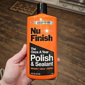 Puede incluir: Una botella naranja de Nu Finish Polish & Sealant, 473 ml. La etiqueta incluye el texto "3 en 1 + Tecnología Cerámica" y "The Once A Year Polish & Sealant". La botella tiene una tapa negra.