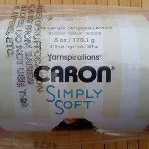 Può includere: Un gomitolo di filato rosa Caron Simply Soft con un'etichetta bianca che recita "100% Acrilico / Acrylique / Acrílico", "Peso Netto - Poids Net - Peso Neto", "6 oz / 170,1 g", "315 yds / vgs / yds / 288 m", "Yarnspirations™", "CARON®", "SIMPLY SOFT®".