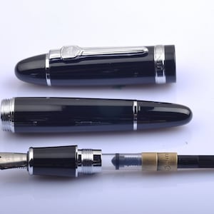 May include: A black fountain pen with a silver trim and a clear ink cartridge. The pen is in three pieces: the cap, the barrel, and the nib and ink cartridge assembly.