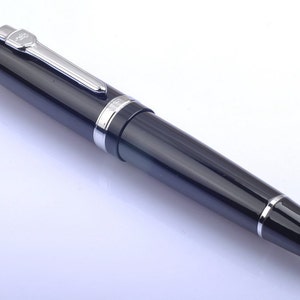 May include: A black fountain pen with a silver trim and a clear ink window. The pen has a cap that is attached to the body with a clip.