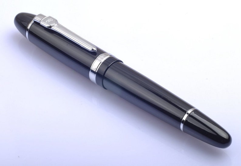 May include: A black fountain pen with a silver trim and a clear ink window. The pen has a cap that is attached to the body with a clip.