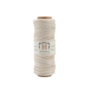 May include: A spool of natural-colored hemp cord. The cord is tightly wound around a cardboard core. A label with the brand name "Hemptique" and other text is wrapped around the spool.