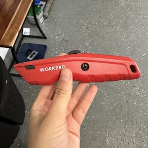 Puede incluir: Un cuchillo de uso general rojo con mango negro y hoja plateada. El cuchillo tiene la palabra "WORKPRO" impresa en el lateral.