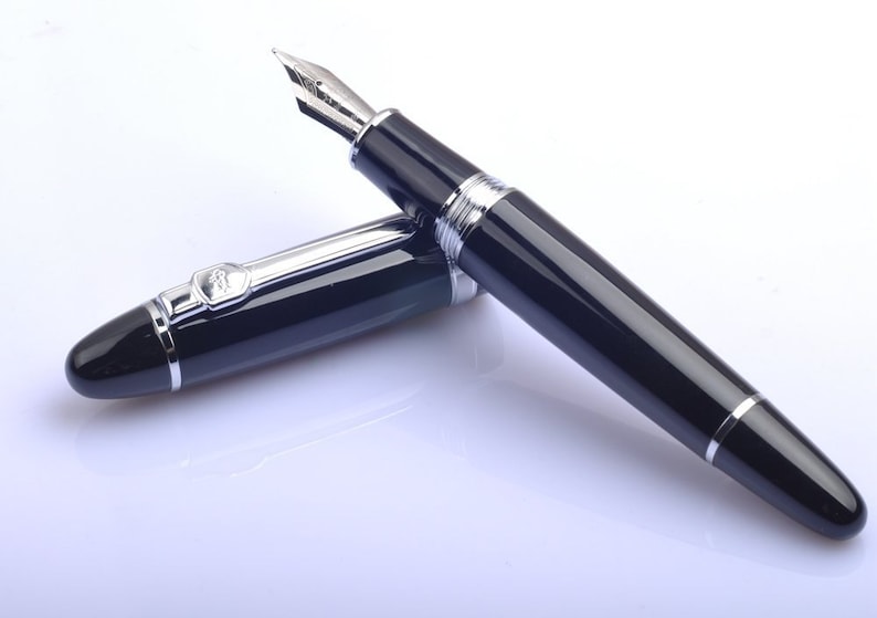 May include: A black fountain pen with silver accents and a fine nib. The pen is lying on a white surface.