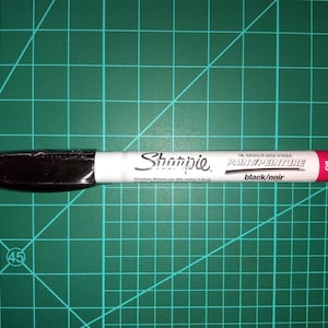 Könnte beinhalten: Ein weißer Sharpie Öl-basierter Farbmarker mit schwarzer Beschriftung "PAINT/PEINTURE black/noir" und einem rosa Etikett mit der Aufschrift "OIL BASED".