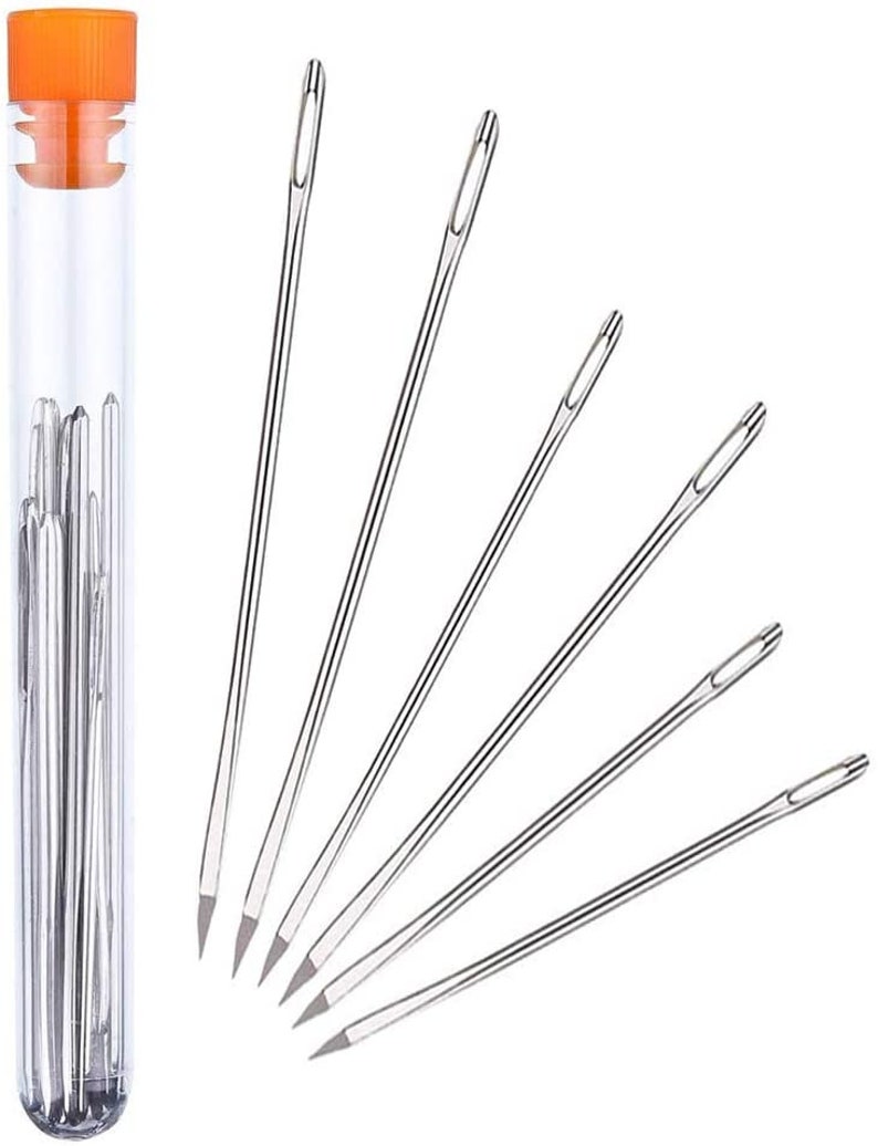 May include: A clear plastic tube filled with silver sewing needles. The tube has an orange lid. Six needles are arranged in a fan shape outside the tube.