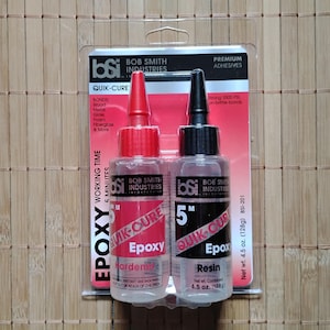May include: Two small bottles of epoxy resin and hardener. The bottles are labeled "Quik-Cure Epoxy" and are 4.5 ounces each. The bottles are red and black with white text.