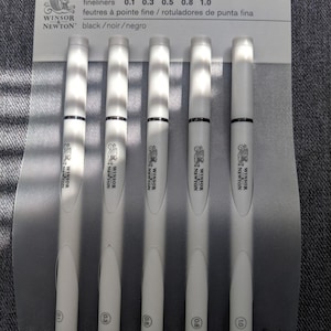 May include: A package of five Winsor & Newton fineliner pens. The pens are white with black accents and have varying tip sizes: 0.1, 0.3, 0.5, 0.8, and 1.0. The packaging includes the brand name and the words "fineliners" and "black/noir/negro".