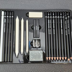 May include: A black art set with charcoal pencils, sketch pencils, blending stumps, a pencil sharpener, and an eraser. The set includes pencils labeled "CHARCOAL PENCIL" and "GETHPEN SKETCH PENCIL". The pencils are arranged in a black plastic tray.