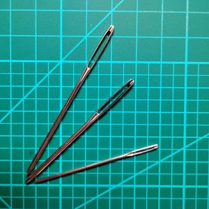Peut inclure: Trois aiguilles à coudre argentées sur un tapis de coupe vert.