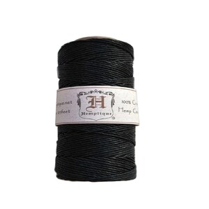 Op de afbeelding: Een spoel met zwarte hennepkoord, 100% natuurlijk, met een label met de tekst "Hemptique" en "100% Hemp Cord".