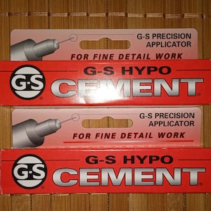 Może przedstawiać: Dwa opakowania kleju G-S Hypo Cement z precyzyjnym aplikatorem do precyzyjnych prac. Opakowania są czerwone i białe z logo G-S i tekstem "G-S Hypo Cement".