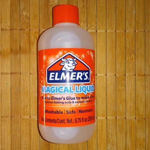 May include: A clear plastic bottle of Elmer's Magical Liquid glue with an orange label. The label features a white cow and the text "ELMER'S MAGICAL LIQUID" in blue and white. The bottle is 8.75 fluid ounces (258 ml).
