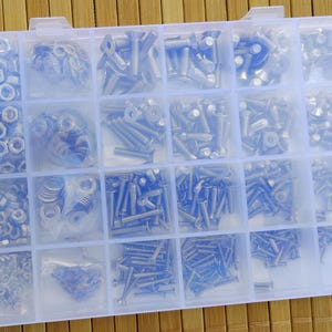 May include: A rectangular, translucent plastic storage organizer box featuring twenty-four individual compartments filled with an assortment of silver-colored metal hardware, including various sizes of screws, bolts, nuts, and flat washers.