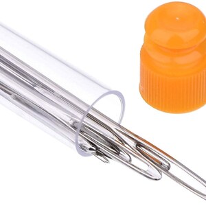 Op de afbeelding: Een transparante plastic buis met een set zilveren naalden. De buis heeft een oranje plastic dop.
