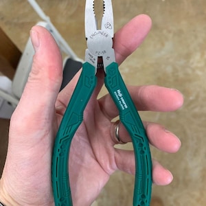 May include: Engineer PZ-58 screw pliers with green handles. The pliers are made in Japan and feature the text "ENGINEER" and "Neji-saurus SCREW PLIERS". The pliers are held open in a hand.