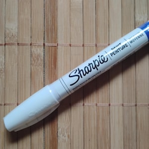 Könnte beinhalten: Weißer Sharpie-Farbstift mit schwarzer Beschriftung und den Worten "Paint/Peinture" und "Moyenne" auf dem Schaft.
