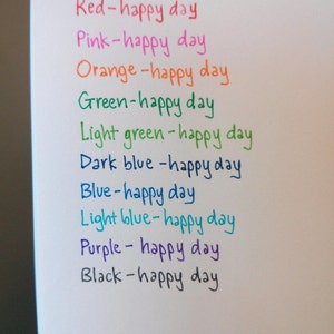 K&ouml;nnte beinhalten: Ein wei&szlig;es Blatt Papier mit dem Satz "happy day" in verschiedenen Farben geschrieben, darunter Rot, Rosa, Orange, Gr&uuml;n, Hellgr&uuml;n, Dunkelblau, Blau, Hellblau, Lila und Schwarz.