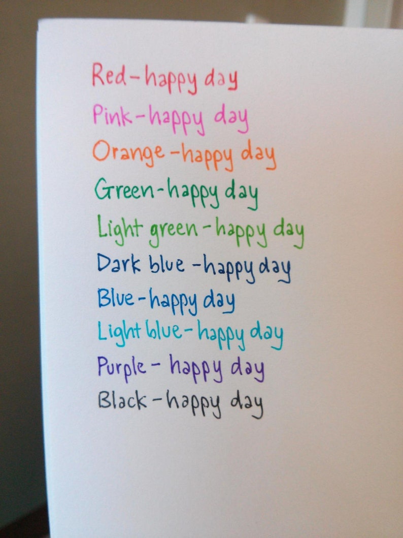 K&ouml;nnte beinhalten: Ein wei&szlig;es Blatt Papier mit dem Satz "happy day" in verschiedenen Farben geschrieben, darunter Rot, Rosa, Orange, Gr&uuml;n, Hellgr&uuml;n, Dunkelblau, Blau, Hellblau, Lila und Schwarz.