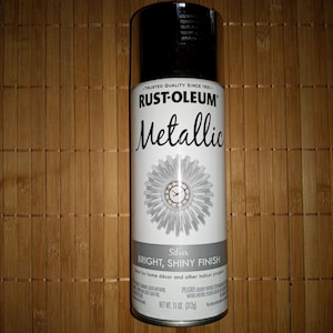 Pode incluir: Uma lata de tinta spray prateada metálica Rust-Oleum. A lata é prateada com uma tampa preta e um rótulo branco. O rótulo diz "Rust-Oleum Metallic" em letras pretas e "Silver Bright, Shiny Finish" em letras pretas menores. A lata é de 312 g (11 oz).