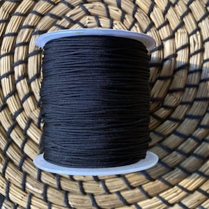 May include: A spool of black elastic cord, wound tightly on a white plastic spool. The cord is smooth and appears to be strong.