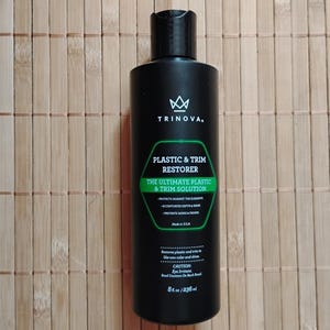 May include: A black plastic bottle of car care product called "Plastic & Trim Restorer" by Trinova. The bottle is labeled "The Ultimate Plastic & Trim Solution" and says it protects against the elements and restores color and shine. The bottle is 8 fl oz / 236 ml.