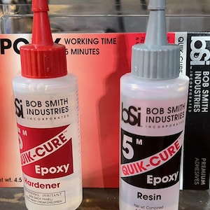 May include: Two clear plastic bottles of Bob Smith Industries 5 Minute Quik-Cure Epoxy. The bottle on the left is labeled "Hardener" and the bottle on the right is labeled "Resin". Both bottles have a net weight of 4.5 ounces.