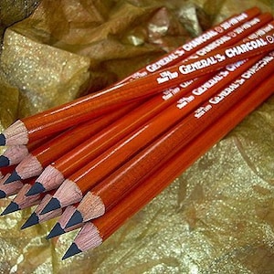 May include: A close-up of a bundle of red charcoal pencils with white lettering that reads "General's Charcoal 5B/7B Hard".