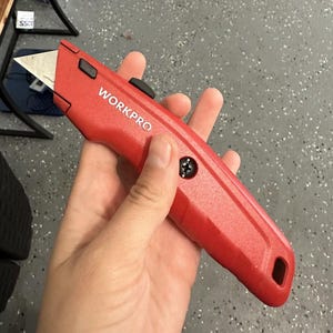 Puede incluir: Un cuchillo de uso general rojo con una hoja plateada y un mango negro. El cuchillo tiene la palabra "WORKPRO" impresa en el mango.