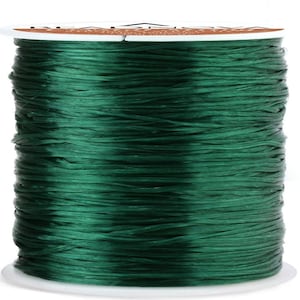 May include: A spool of dark green elastic cord. The cord is wound tightly around a white spool with a brown label.