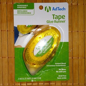 May include: A yellow tape glue runner dispenser with the text "Tape Glue Runner Removable" on the front. The packaging is green and white and says "AdTech Tape Glue Runner". It also says "Removable, Refillable, Rechargeable, Instant Bond, No Mess, Acid Free".