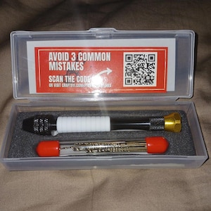 May include: A clear plastic case containing a black and gold hand drill and a set of drill bits. The case has a label that reads "AVOID 3 COMMON MISTAKES" and a QR code. The label also says "SCAN THE CODE" and "OR VISIT CRAFT911.COM/PINHOLE-MISTAKES"