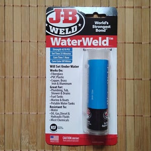 Puede incluir: Un tubo azul de adhesivo JB Weld WaterWeld con una etiqueta blanca. La etiqueta dice "World's Strongest Bond" y "Will Set Under Water". La etiqueta también enumera la resistencia, el tiempo de fraguado, el tiempo de curado y el color de curado del adhesivo.