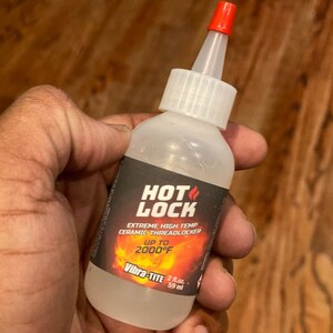 May include: A clear bottle of Vibra-TITE HOT LOCK ceramic threadlocker with a red cap. The label reads "EXTREME HIGH TEMP" and "UP TO 2000°F". The bottle contains 2 fl. oz. or 59 ml of product.