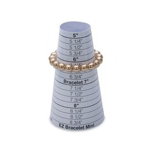 Op de afbeelding: Een witte papieren kegel met een zwarte, geprinte schaal voor het meten van armbandmaten in inches. De schaal loopt van 5 tot 8 3/4 inch. Een gouden armband is op de kegel geplaatst op de 6 3/4 inch markering. De tekst "EZ Bracelet Mini" is gedrukt op de bodem van de kegel.